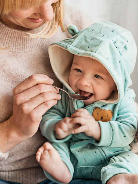 a mother feeding her baby, who is wearing a light green hoodie.