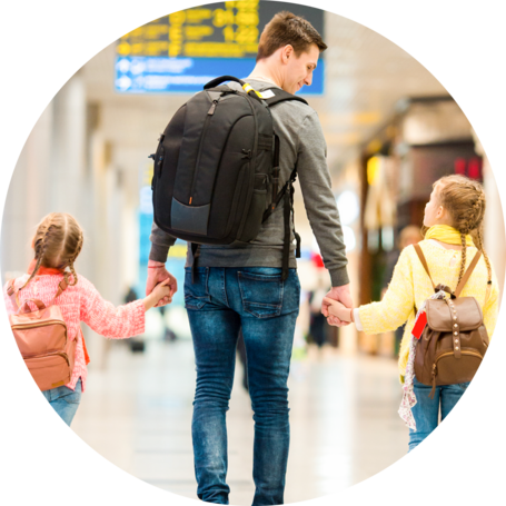 A man holding hands with two young girls, walking together in an airport terminal.